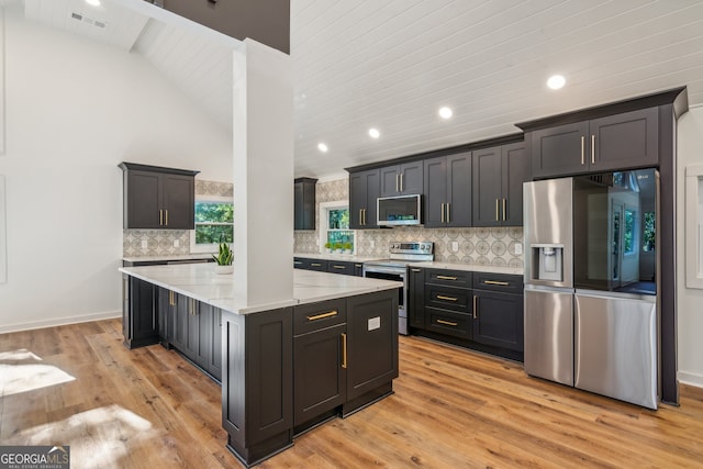 kitchen with light wood-type flooring, appliances with stainless steel finishes, backsplash, light stone countertops, and wood ceiling