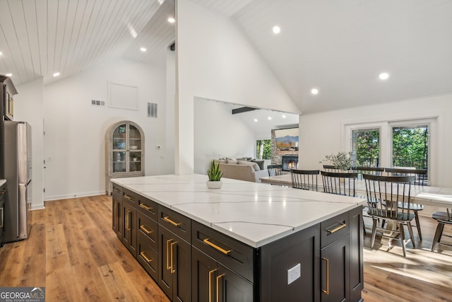 kitchen with wood ceiling, a fireplace, high vaulted ceiling, light wood-type flooring, and stainless steel fridge