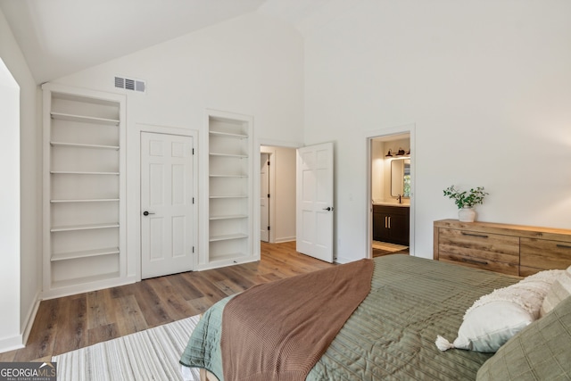 bedroom with ensuite bathroom, high vaulted ceiling, and wood-type flooring