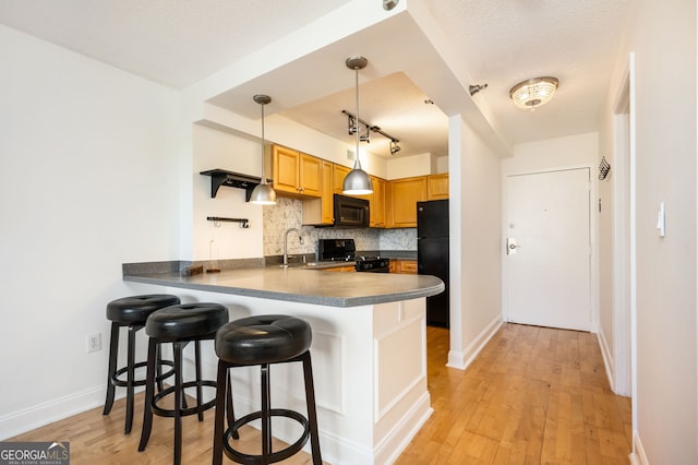 kitchen featuring backsplash, a kitchen breakfast bar, black appliances, decorative light fixtures, and kitchen peninsula