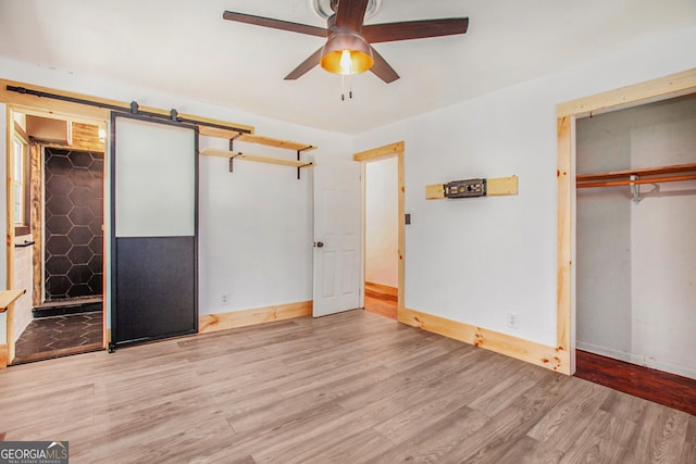 unfurnished bedroom with ceiling fan, a barn door, light wood-type flooring, and connected bathroom