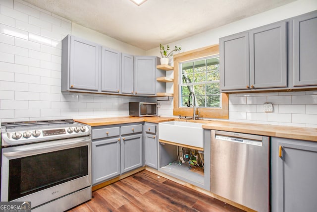 kitchen featuring gray cabinetry, dark hardwood / wood-style floors, decorative backsplash, butcher block counters, and stainless steel appliances