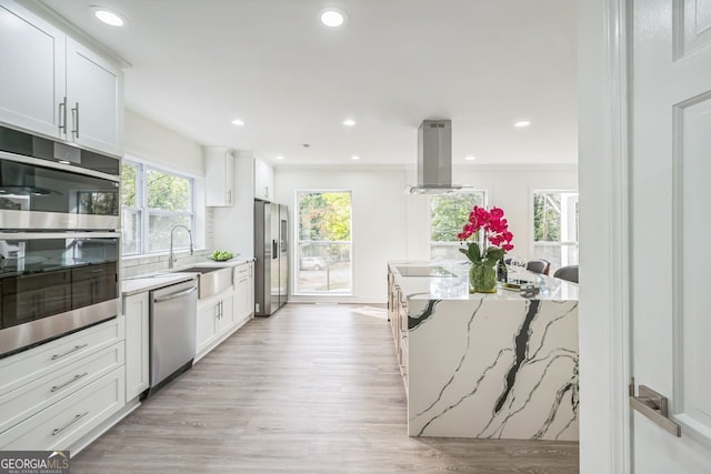 kitchen featuring white cabinetry, light stone countertops, light hardwood / wood-style floors, island range hood, and appliances with stainless steel finishes