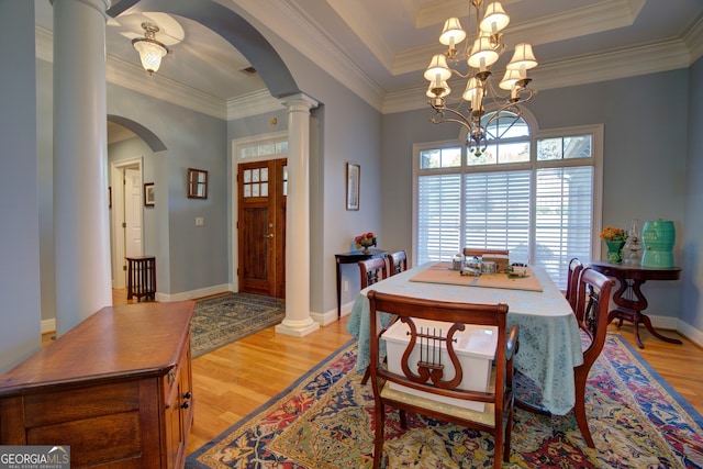 dining area with decorative columns, a tray ceiling, crown molding, a notable chandelier, and light hardwood / wood-style flooring