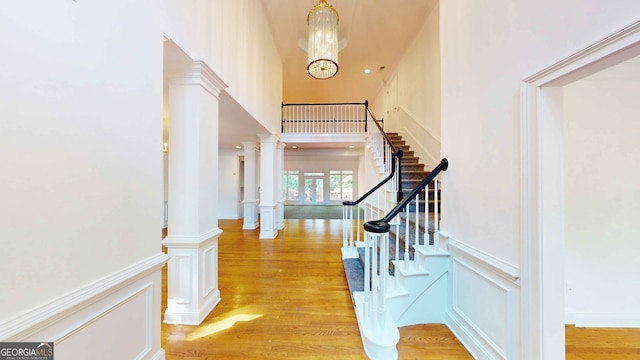 foyer featuring ornate columns, light hardwood / wood-style flooring, a chandelier, and a high ceiling