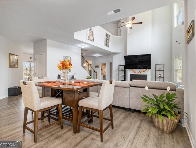 dining space with a high ceiling, ceiling fan, and light hardwood / wood-style flooring