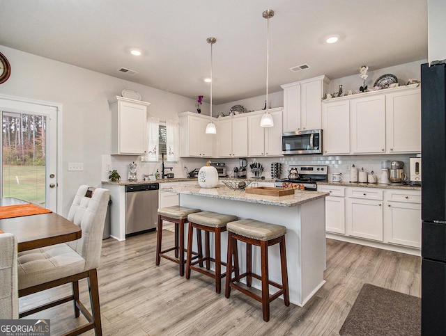 kitchen featuring hanging light fixtures, white cabinets, stainless steel appliances, and a center island