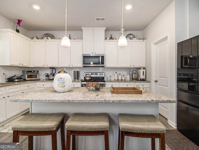 kitchen with white cabinetry, appliances with stainless steel finishes, hanging light fixtures, and a center island