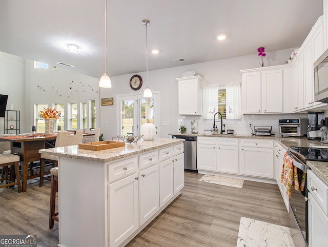 kitchen with light hardwood / wood-style floors, sink, appliances with stainless steel finishes, hanging light fixtures, and white cabinets