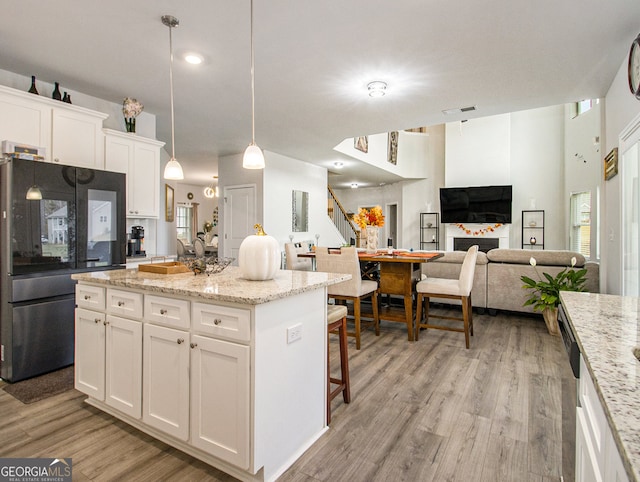 kitchen with black refrigerator, white cabinets, hanging light fixtures, light stone countertops, and light wood-type flooring