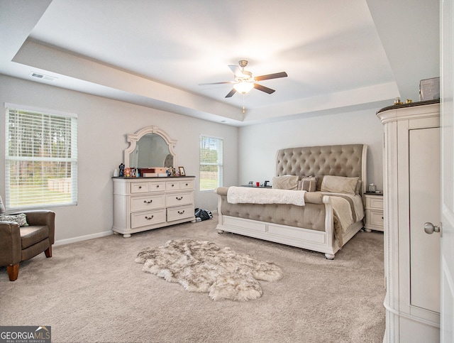 bedroom with light colored carpet, ceiling fan, and a tray ceiling