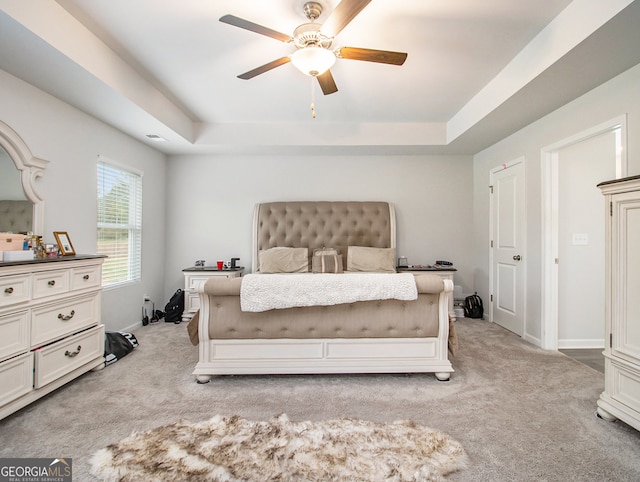 bedroom with light colored carpet, ceiling fan, and a raised ceiling