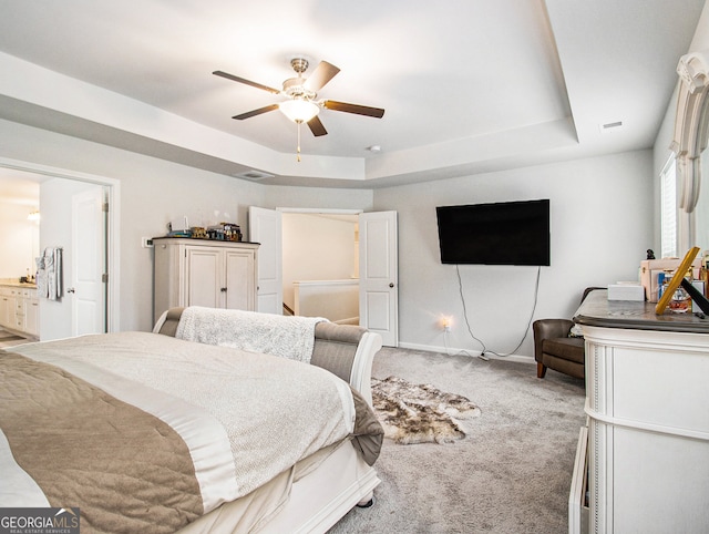 carpeted bedroom featuring a raised ceiling, ceiling fan, and ensuite bathroom