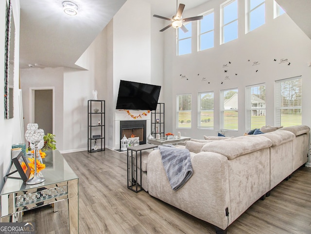 living room with a towering ceiling, ceiling fan, plenty of natural light, and light hardwood / wood-style flooring