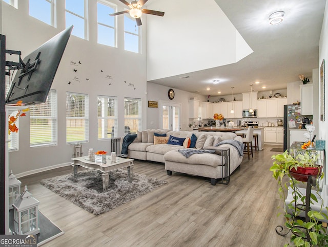 living room with light hardwood / wood-style floors, ceiling fan, and a high ceiling