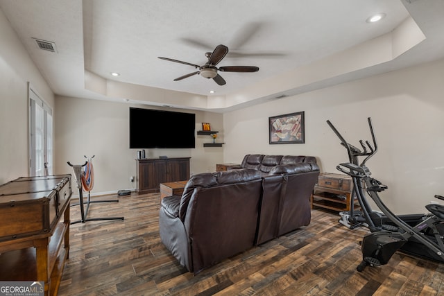 living room with dark wood-type flooring, ceiling fan, and a tray ceiling