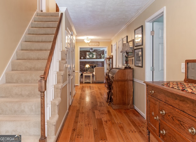 hall featuring a textured ceiling, ornamental molding, and light hardwood / wood-style flooring