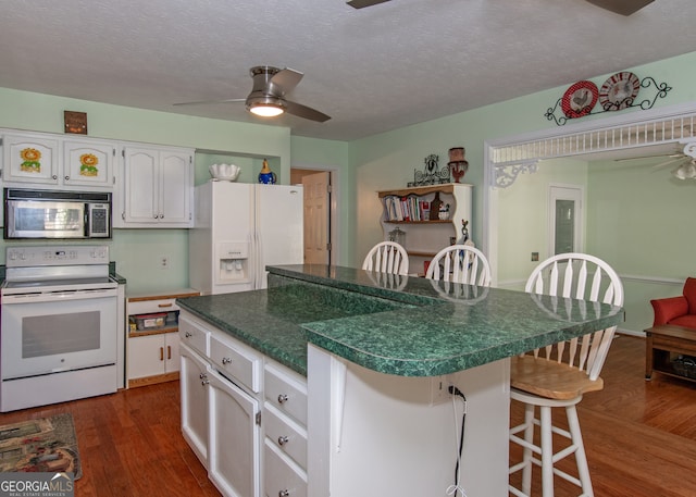 kitchen with white appliances, a kitchen island, white cabinets, dark wood-type flooring, and a breakfast bar area