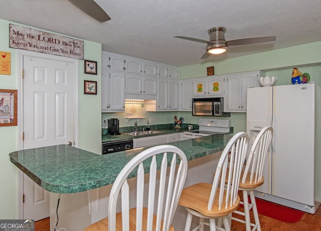 kitchen with white appliances, sink, a textured ceiling, light hardwood / wood-style floors, and a breakfast bar area