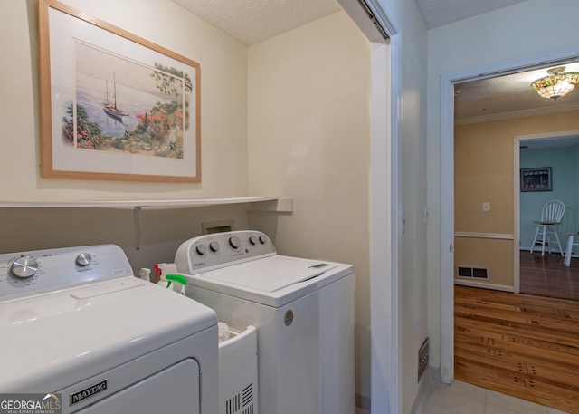 clothes washing area with light hardwood / wood-style floors, a textured ceiling, and washing machine and clothes dryer