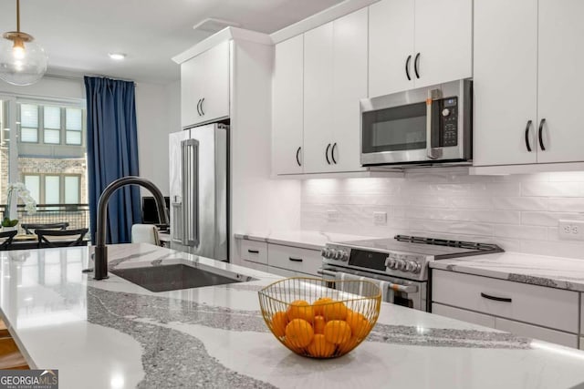 kitchen with hanging light fixtures, light stone countertops, sink, and appliances with stainless steel finishes