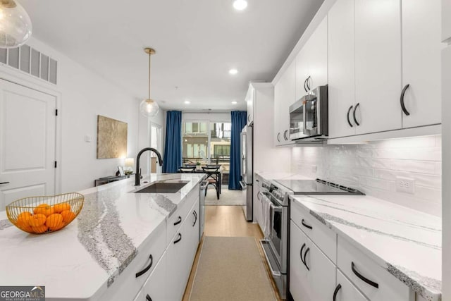 kitchen with pendant lighting, sink, appliances with stainless steel finishes, white cabinetry, and a kitchen island with sink