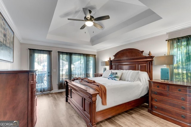 bedroom with light hardwood / wood-style flooring, a tray ceiling, crown molding, and ceiling fan