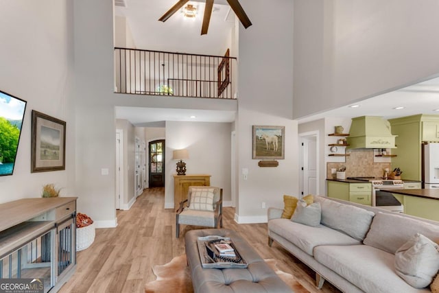 living room featuring a towering ceiling, light wood-type flooring, and ceiling fan