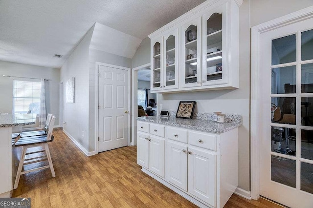 kitchen featuring white cabinets, light stone counters, a textured ceiling, and light hardwood / wood-style floors