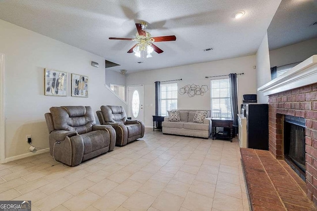 living room featuring ceiling fan, a textured ceiling, light tile patterned floors, and a brick fireplace