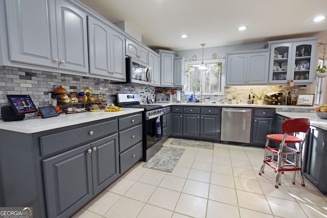 kitchen with appliances with stainless steel finishes, hanging light fixtures, gray cabinets, and light tile patterned floors