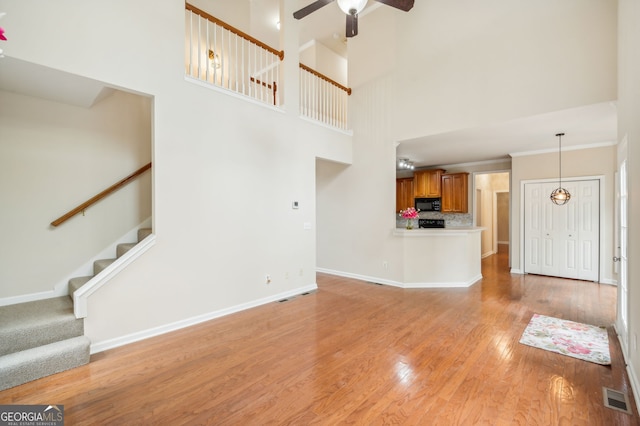 unfurnished living room featuring ceiling fan, a high ceiling, and light wood-type flooring