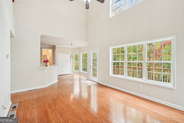 unfurnished living room featuring ceiling fan, a towering ceiling, and light wood-type flooring