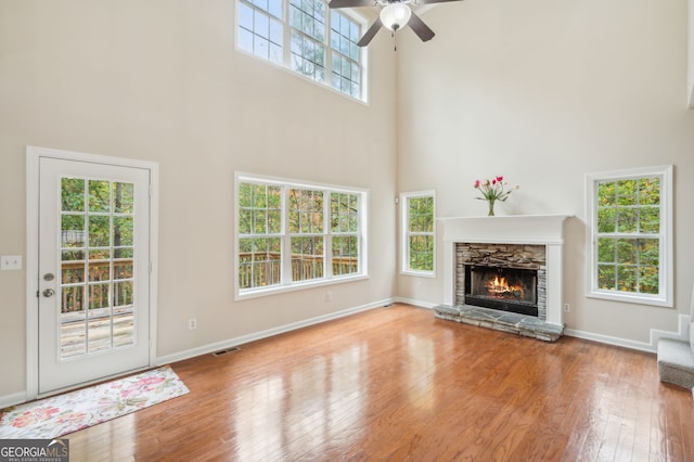 unfurnished living room featuring hardwood / wood-style floors, a stone fireplace, a towering ceiling, and ceiling fan