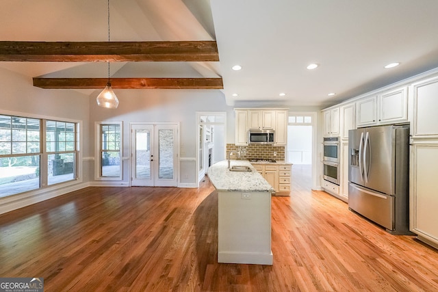 kitchen with hanging light fixtures, stainless steel appliances, light stone counters, backsplash, and light hardwood / wood-style floors