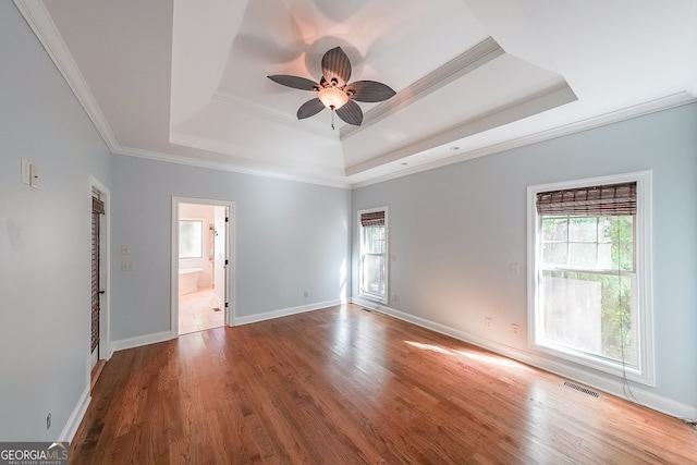 empty room with hardwood / wood-style floors, a tray ceiling, and a healthy amount of sunlight