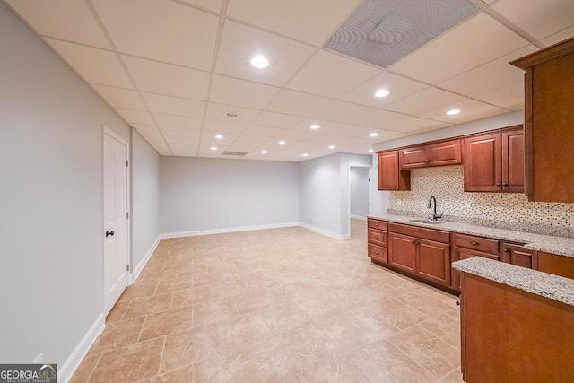 kitchen with tasteful backsplash, light stone counters, sink, and a drop ceiling