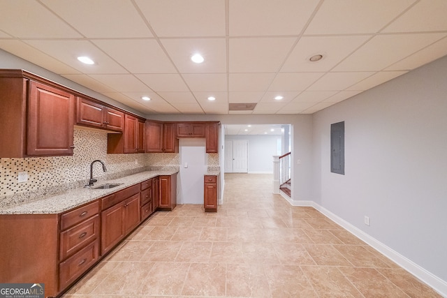 kitchen featuring tasteful backsplash, light stone counters, a drop ceiling, and sink