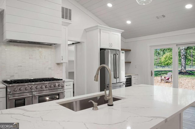 kitchen featuring sink, high quality appliances, white cabinetry, lofted ceiling, and light stone counters