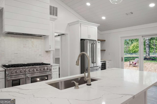kitchen with a sink, backsplash, vaulted ceiling, white cabinets, and appliances with stainless steel finishes