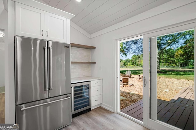 kitchen featuring high end refrigerator, white cabinetry, light hardwood / wood-style floors, vaulted ceiling, and beverage cooler