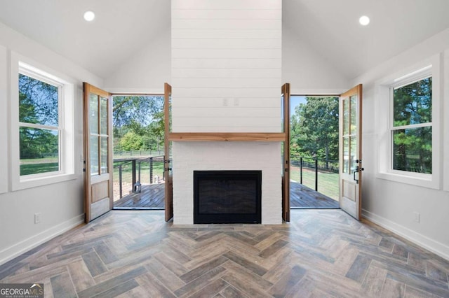 unfurnished living room with parquet flooring, high vaulted ceiling, a large fireplace, and plenty of natural light