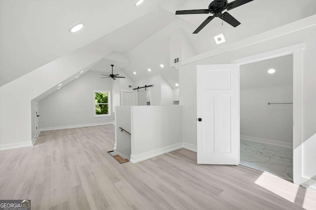 additional living space with light hardwood / wood-style floors, vaulted ceiling, a barn door, and ceiling fan