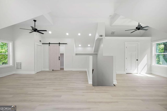 unfurnished living room with a barn door, light hardwood / wood-style flooring, high vaulted ceiling, and a healthy amount of sunlight