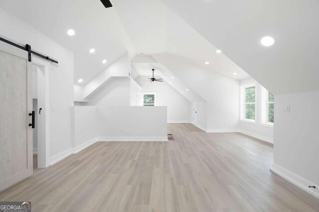 additional living space featuring wood finished floors, a barn door, a ceiling fan, and vaulted ceiling
