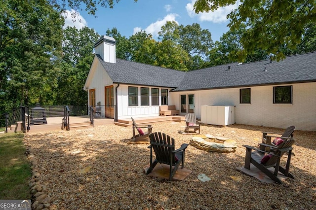 back of property with a deck, roof with shingles, board and batten siding, and an outdoor fire pit