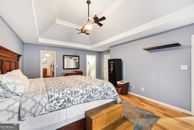 bedroom featuring a spacious closet, a tray ceiling, a closet, ceiling fan, and light hardwood / wood-style floors