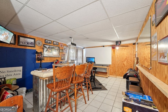 bar with a drop ceiling, wood walls, and light tile patterned flooring