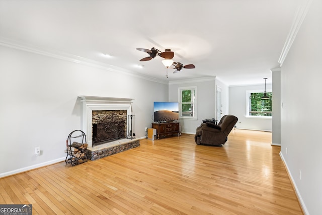 living room featuring ornamental molding, a stone fireplace, light wood-type flooring, and ceiling fan