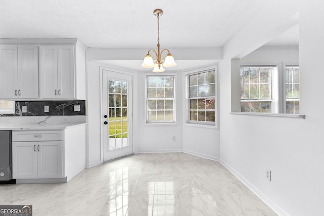 unfurnished dining area featuring a healthy amount of sunlight, a textured ceiling, and an inviting chandelier